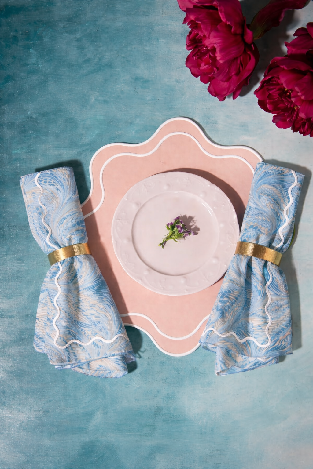 Dinner setting with pink plate, Florentine Marbled napkins, and pink flowers on a blue background